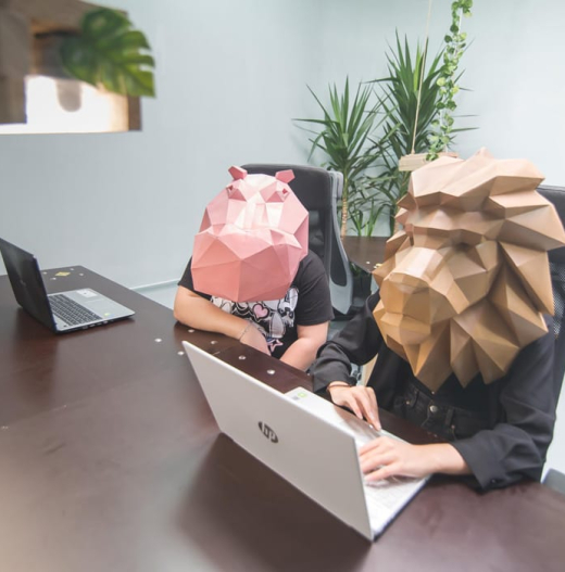 Two people sitting at a desk with paper mask of a lion and a hipo on their heads, at jungle coworking.